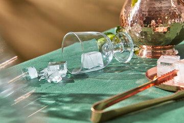 Ice falling out of glass on table with copper jug.