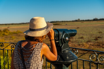 A young woman with binoculars looking at the horses grazing in the Doñana park next to the El...