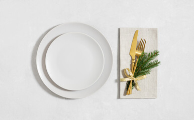 Empty plate with golden cutlery and a fir branch on a gray background. Christmas dinner. Copy space, top view, flat lay.
