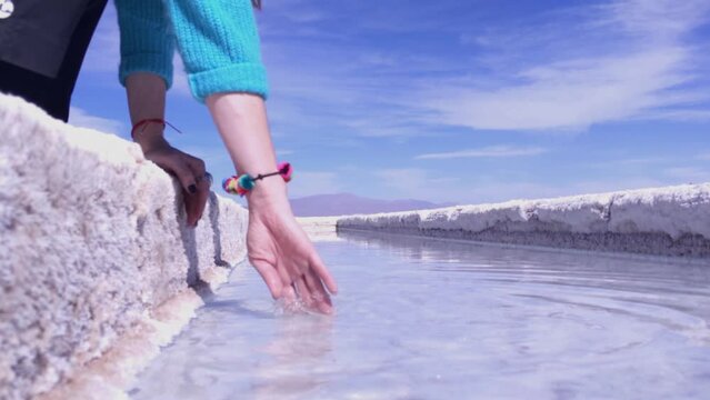 Woman Touching Salt Brine in Evaporation Pond, Salinas Grandes Salt Flats, Jujuy, Argentina - Close Up