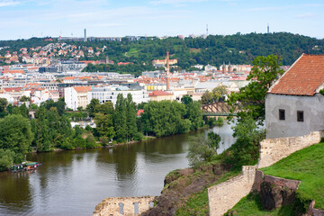 Fototapeta na wymiar Modern day skyline of Vltava River and beyond in Prague in the Czech Republic taken from Vysehrad ramparts looking toward the river. The red brick wall is part of the old defense system. 