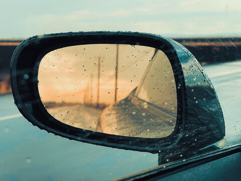 Close-up of raindrops on a sport car mirror with reflection of a wet road and power lines in California
