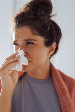 Woman wiping nose at home covered with blanket