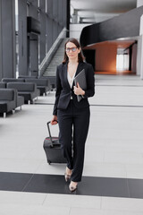 business tourism, business woman in a formal suit with a smartphone in a business center or airport with a suitcase goes on a business trip. Work in a corporation as a marketing financier or lawyer. a