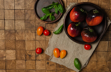 Colorful tomatoes, red, yellow, orange, purple with basil leaves on vintage wood background. Top view, flat lay, copy space for text