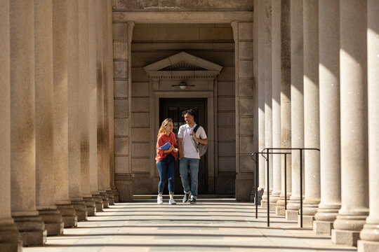 Two Friends University Students walk down long corridor on campus 