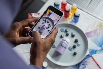 Crop man taking photo of paint and berries on plate
