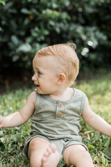 Cute baby boy sitting on the grass turned away