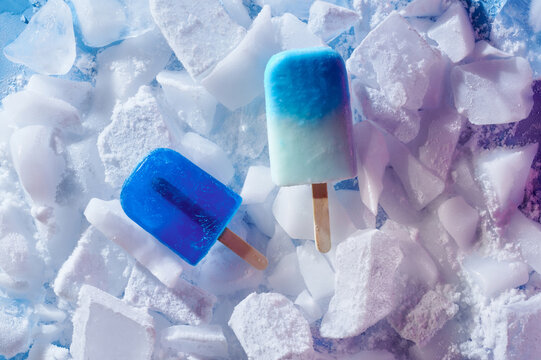 Homemade blue popsicles on ice over color background