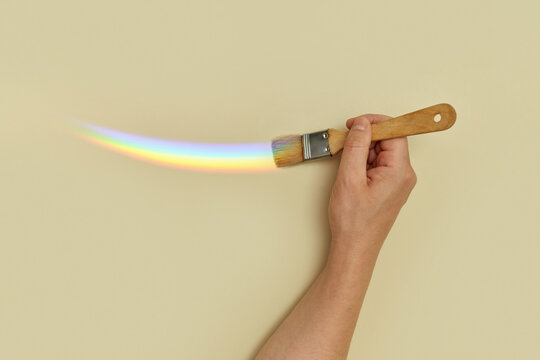 Person's hand painting rainbow on beige wall.