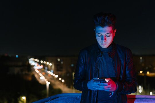 Serious guy using smartphone on bridge at night