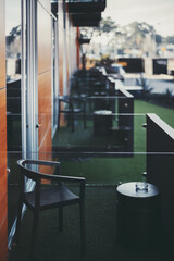 A vertical shot with a shallow depth of field and a selective focus on the chair placed on the modern balcony of a hotel with a row of identical balconies in the defocused background