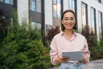 Fototapeta premium Smiling confident asian woman wearing stylish eyeglasses holding digital tablet looking at camera, copy space 