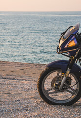 Fototapeta na wymiar A motorcycle on the Black Sea coast, on a beach made of shell rock, in soft sunset lighting