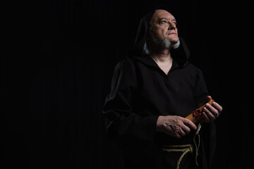 senior monk with rolled manuscript looking away isolated on black.