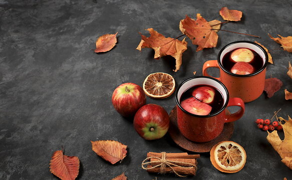 Autumn composition with colored enamel mugs with hot autumn drink, mulled wine with apples and fallen leaves on a rusty table, banner, hello autumn concept,