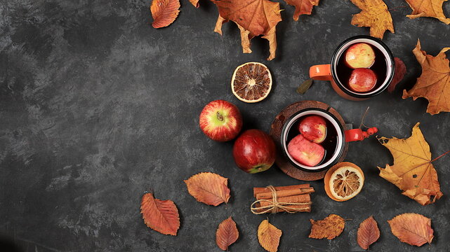 Autumn composition with colored enamel mugs with hot autumn drink, mulled wine with apples and fallen leaves on a rusty table, banner, hello autumn concept,