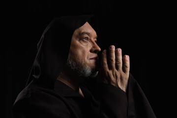 side view of medieval monk with praying hands near face isolated on black.