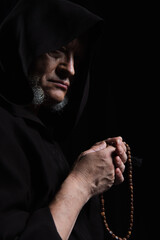 medieval monk in hood holding rosary isolated on black.
