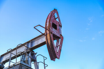 An abandoned oil or gas rocking machine against a blue sky, exhausted resource. A clogged field of...