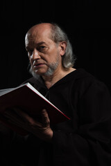 senior priest with holy bible looking at camera isolated on black.