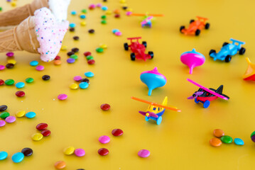 dried ice cream, colorful chocolates and plastic toys on a yellow background