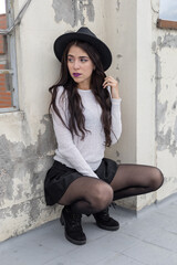 natural makeup of woman squatting posing, lifestyle, wearing a hat, sweater and skirt, person and fashion portrait