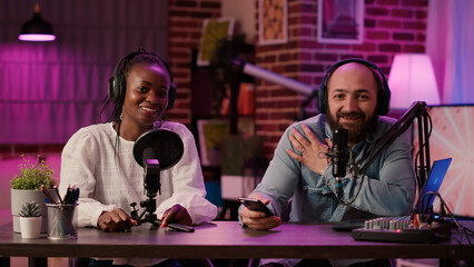 Diverse team of online radio hosts recording podcast review for smartphone streaming audio with...