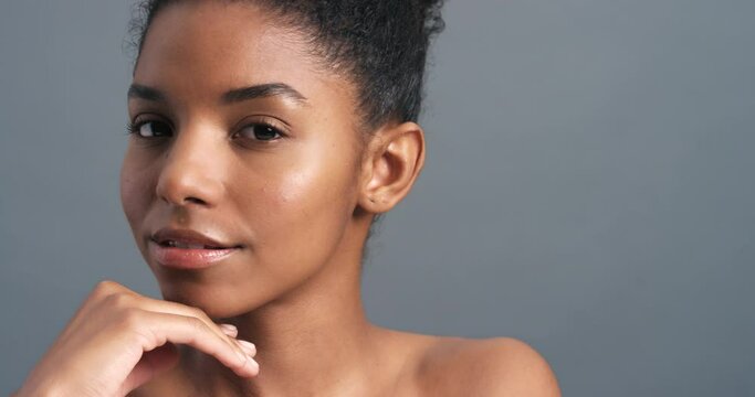 Model touch face, sexy wink and flirty smile against studio background or wall. Nude black woman rub skin with hand, make flirting gesture with eye and happy facial expression against grey backdrop.