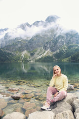 Fototapeta na wymiar Poland - September, 2022: beautiful blonde sits on the background of the lake Morskie oko