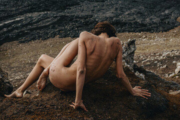 Naked woman sitting in front of black lava river in Iceland 