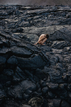 Nude woman sitting on black solid lava field in Iceland 