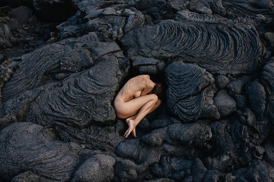 Nude woman lying in fetal position on black solid lava in Iceland 
