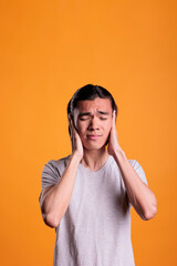 Young asian man covering ears with hands, hear no evil, three wise monkeys moral concept. Scared...