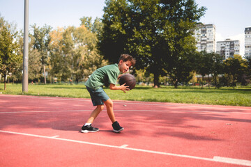 Obraz premium Young Caucasian teenage boy playing basketball. He is wearing summer outfit with shorts and t-shirt.