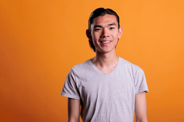 Young joyful smiling asian man portrait, teenage guy looking at camera, front view. Cheerful teen with positive facial expression and smile, handsome photogenic person medium shot