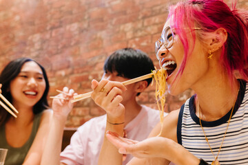 Young chinese woman eating noodles with friends