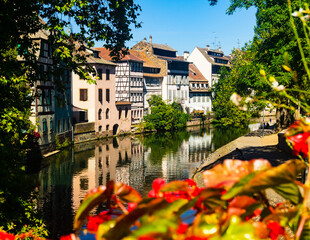 Fototapeta premium Charming view of residential half-timbered buildings along canals of Strasbourg. Summer streets decorated with bloomy flowers.