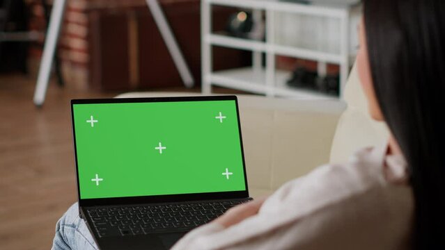 Woman having laptop with green screen chroma key template display while sitting on sofa at home. Person with computer having mockup isolated background while in apartment.