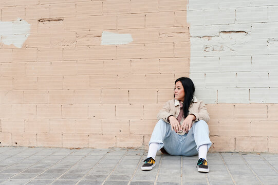 Young woman sitting against a wall outside