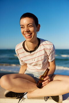Young woman with beer sitting on border near sea