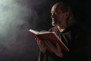 mysterious monk with holy bible looking away on black with smoke.