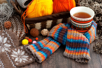 Yarn, a knitted scarf and a mug of hot tea. Wicker basket with yarn, a cup of tea, mittens, a scarf and a hat to keep warm in the cold season. 