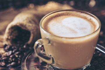 Coffee cup latte art and cappuccino with heart-shaped made from milk on the wood table with roasting coffee beans.