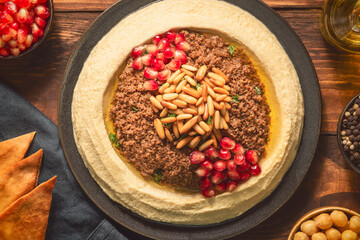 Arabic cuisine; Traditional creamy hummus dip with ground beef. Topped with olive oil, fresh pomegranate seeds, roasted pine nuts and parsley. Top view with close up.