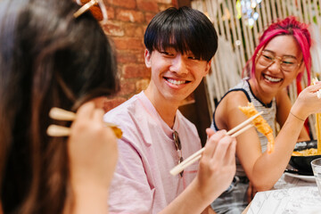 Cheerful chinese friends eating sushi in restaurant