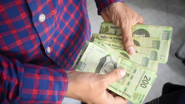 Manos de un joven hombre contando billetes de doscientos pesos mexicanos 