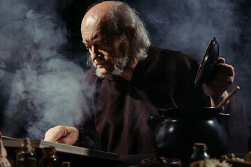 medieval alchemist reading magic cookbook while preparing potion at night on black background with...