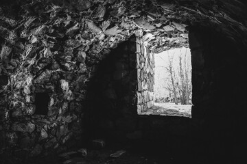 Dungeon and tunnel in Sveaborg fortress. Helsinki, Finland. Atmospheric sightseeing. Rays of light shining into empty old cellar. Trees outside. Texture and structure of aged stone walls. Monochrome