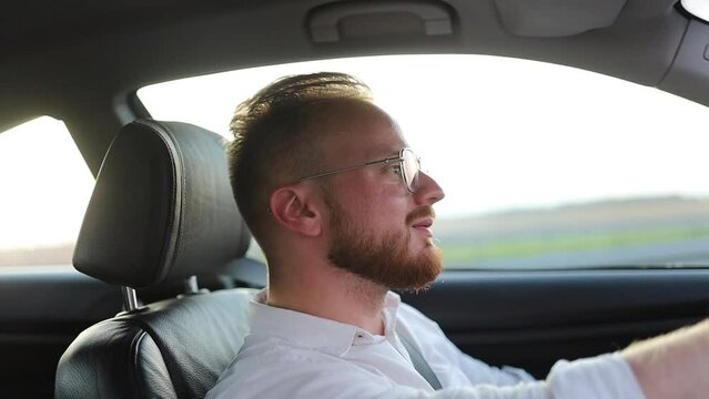 young man is driving along a busy highway in his car and is staring at the road. Man with glasses driving on a sunny day